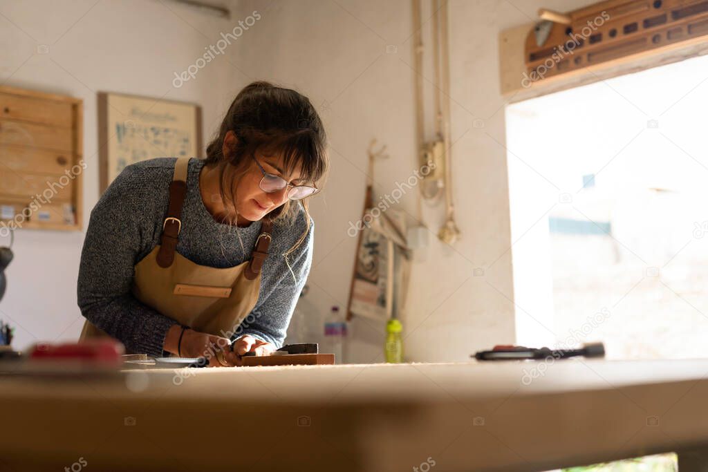 A young female carpenter working as wood designer in a small carpentry workshop. Young business woman handcrafting a piece of timber and designing new house furniture. Entrepreneurs concept lifestyle