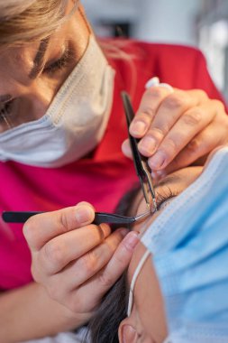 Kirpik uzatma prosedürü. Uzun kirpikli kadın gözü. Kırbaçlar. Maskeyle Tıbbî Kapak.