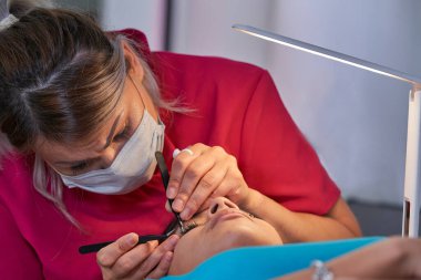 Kirpik uzatma prosedürü. Uzun kirpikli kadın gözü. Kırbaçlar. Maskeyle Tıbbî Kapak.