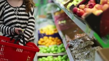 Genç bir kız olgun elmaları bir mağazanın rafında seçiyor.