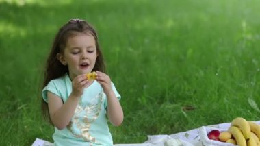 Piknik. Yeşil çimenlikteki küçük bir kız olgun bir kayısı ısırır..