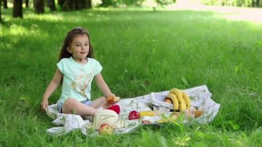 Doğada piknik. Yeşil çimenlikte küçük bir kız dolgulu bir turtayı ısırıyor..