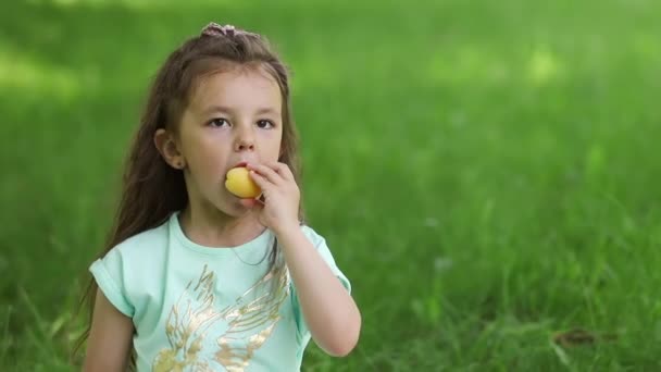 緑の芝生の上の少女は熟したアプリコットを噛んだ 肖像画 — ストック動画