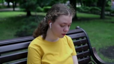 Kamera, elinde telefonla şehir parkındaki bir bankta oturan genç bir kızın yüzünden uzaklaşıyor.