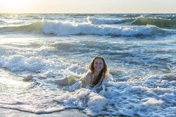 Woman lies in the surf zone in the sea waves at dawn