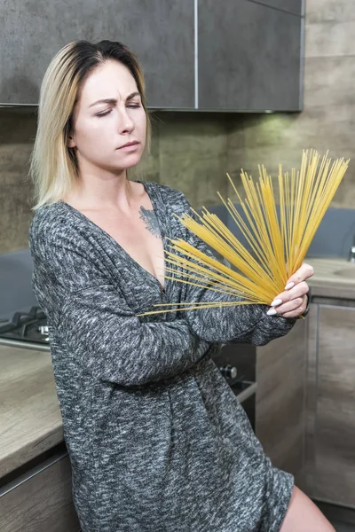 Beautiful woman in the kitchen with spaghetti in the form of a fan in her hand