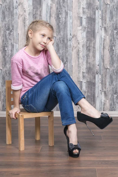 Child in heels sits on a chair — Stock Photo, Image