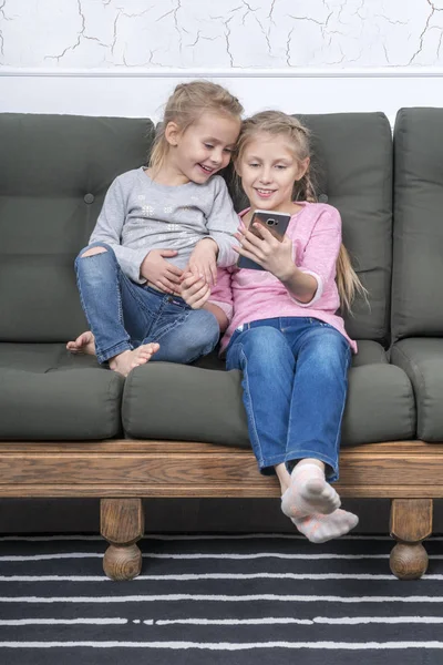 Duas Meninas Sentadas Sofá Estão Olhando Para Tela Smartphone Rindo — Fotografia de Stock