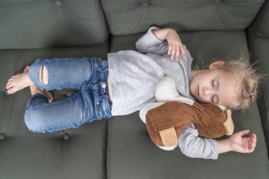 yumuşak bir oyuncakla giysili kanepede uyuyan küçük güzel kız