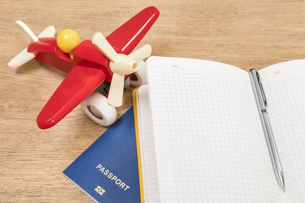 Plane, notebook and passport on wooden table — Stock Photo, Image