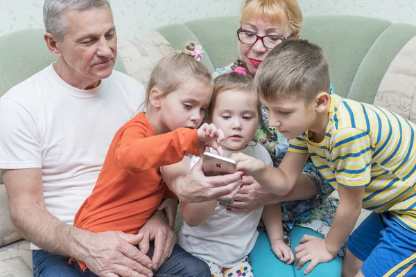 Großeltern mit Enkeln schauen aufs Smartphone — Stockfoto