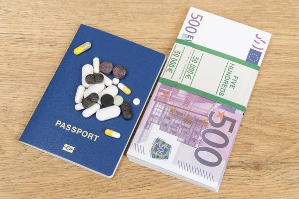 bundle of money and a passport with pills on an old wooden table