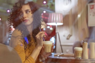 Bir fincan kahve bir kafede pencerenin dışında güzel kıvırcık saçlı bir kadınla