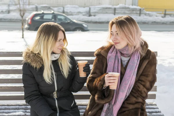 two women drinking coffee on a bench