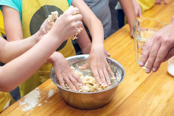 Children knead the dough in a metal bowl on a wooden table