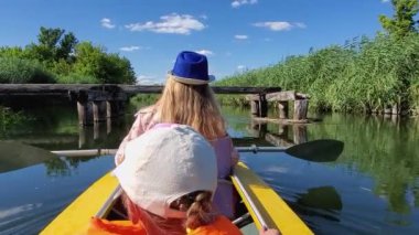Anne ve kızı tahtadan yapılmış köprünün altında yüzen bir kanoda yatıyor.