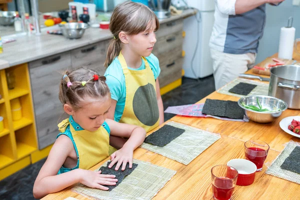 children learn to make sushi standing at the wooden table in the kitchen