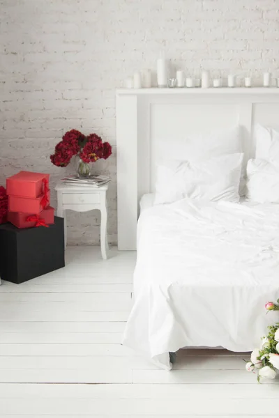 Light cozy room with red and black boxes and flowers. Bedroom. Queen size bad with candles on borders