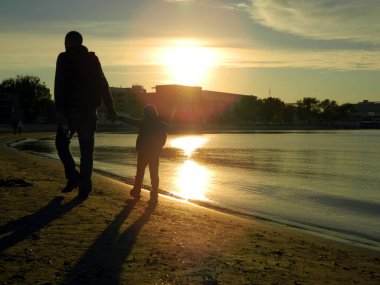 Oğluyla deniz kıyısında yürüyen babanın silueti.