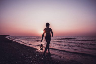 Sahilde gün doğumunda lamba ile genç çocuk