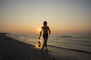 Sahilde gün doğumunda lamba ile genç çocuk