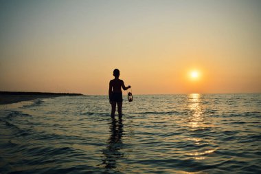 Sahilde gün doğumunda lamba ile genç çocuk