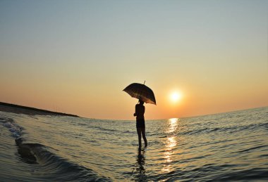 Gün doğumunda plajda şemsiyesi olan genç çocuk 