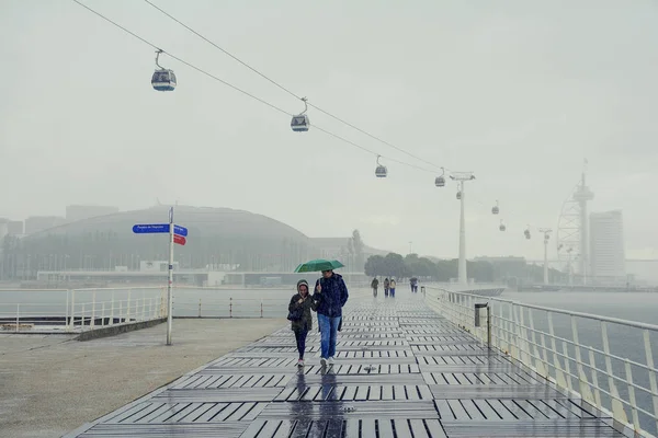 Lizbon, Portekiz - 2 Kasım 2017. Yağmurlu bir günde, Lizbon, Portekiz - Parque das Nacoes - Nation Park teleferik demiryolu ile Tagus nehir kenarında Yürüyüş yolu. Yağmurlu bir günde yürüyen insanlar.  