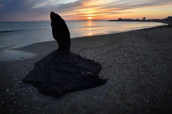 Jonge Vrouw Met Zwarte Kaap Bij Zonsopgang Aan Kust Van — Stockfoto