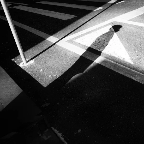 Black and white street photography with shadow of a person waiting to cross the street.