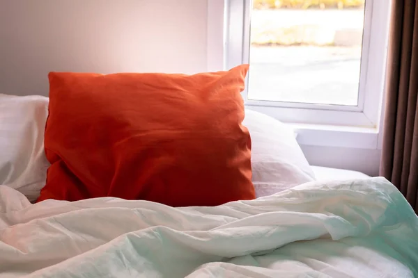 Orange pillow and white blanket on bed in bedroom.