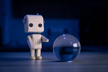 Küçük tahta oyuncak bir robot karanlıkta camdan bir topa bakıyor. Duvar kağıdı, mavi arka plan. loş ışık