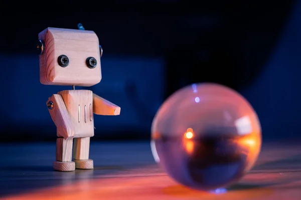 Küçük tahta oyuncak bir robot karanlıkta sihirli bir cam topa bakıyor. Duvar kağıdı, mavi arka plan. loş ışık