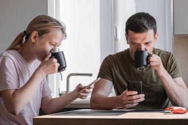 Günaydın, genç aile kahve içer ve akıllı telefonlara bakar. Akıllı telefonların birbirini görmezden gelmesiyle ilgili. Pencereden güneş ışığı geçiyor. İnternet üzerinden mobil uygulamalar kullanarak veya sosyal ağları kontrol ederek. Çift ve teknoloji konsepti. akıllı telefon bağımlısı
