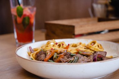 Biftek ve fasulye kabuklu İtalyan spagettisi, bir restorandaki ahşap masada derin bir tabakta havuç..