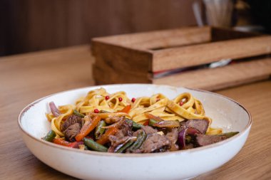 Biftek ve fasulye kabuklu İtalyan spagettisi, bir restorandaki ahşap masada derin bir tabakta havuç..