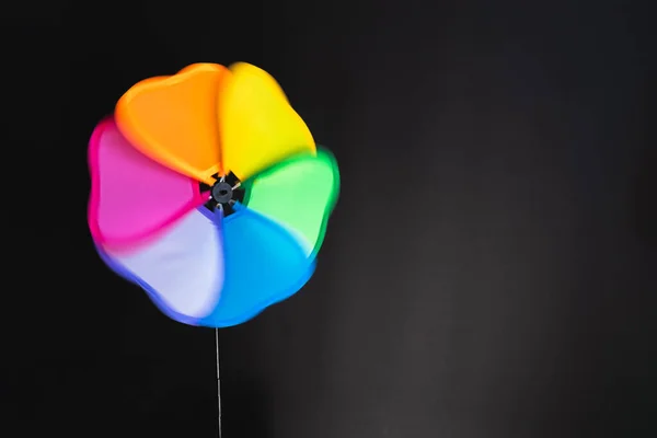 multi-colored wind toy on a black won, the blades leave a blurred trail in the form of a rainbow. LGBTQ+ sign, emblem. space for text