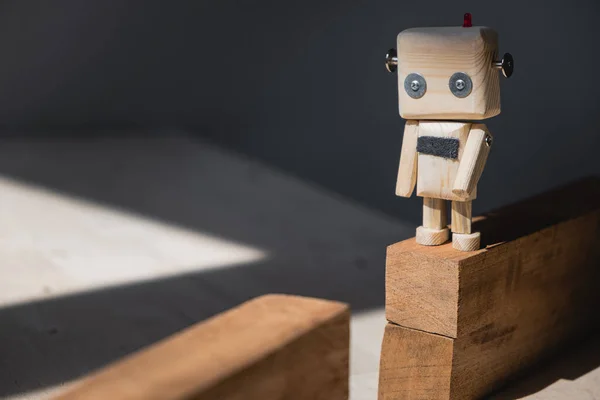 Tahta bloklardan yapılmış bir uçurumun kenarında duran küçük tahta bir robot..