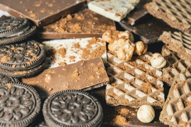 Bir yığın çikolata, malzemeli yuvarlak bisküvi, fındık ve fındık. Hepsi kakao serpilmiş. Dünya Çikolata Günü.