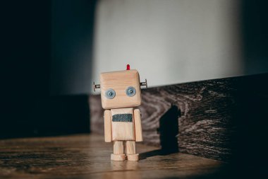 Ahşap oyuncak robot ahşap bir zemin üzerinde bir ışık demeti içinde duruyor ve duvarda bir gölge bırakıyor. Karanlık etrafını sarar.