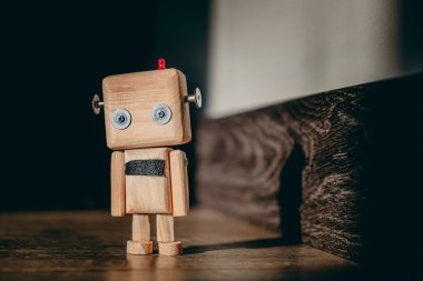 Ahşap oyuncak robot ahşap bir zemin üzerinde bir ışık demeti içinde duruyor ve duvarda bir gölge bırakıyor. Karanlık etrafını sarar.