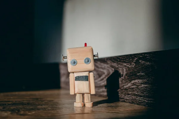 Ahşap oyuncak robot ahşap bir zemin üzerinde bir ışık demeti içinde duruyor ve duvarda bir gölge bırakıyor. Karanlık etrafını sarar.