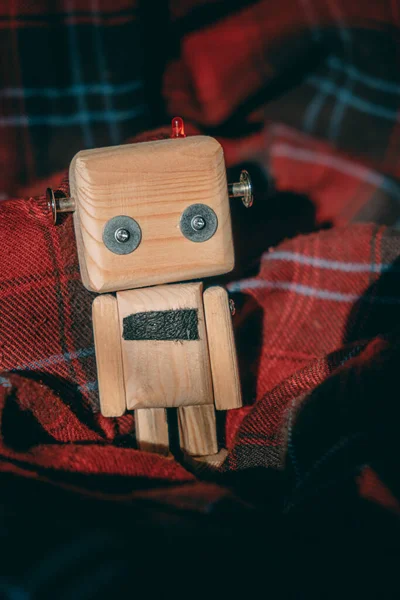 diy wooden toy robot stands wrapped in a cozy checkered red blanket. loneliness concept