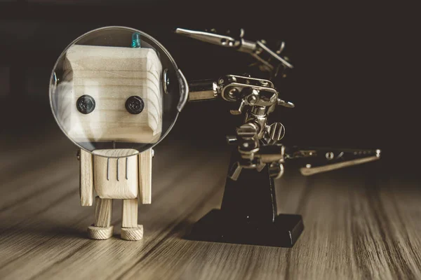 wooden robot android stands on a table under a magnifying glass. metal clamps with a magnifying glass. the face of a robot in the beautifying glass. AI study concept