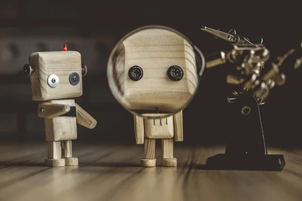 Ahşap robot android büyüteç altındaki bir masanın üzerinde duruyor. Büyüteçle metal kıskaçlar. Güzelleştirici bardaktaki bir robotun yüzü. bilimsel araştırma kavramı