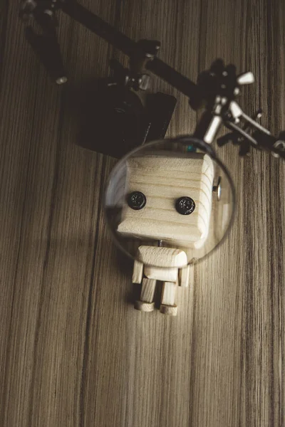 wooden robot android lies on the table under a magnifying glass. third hand of a scientist with a magnifying glass. AI development