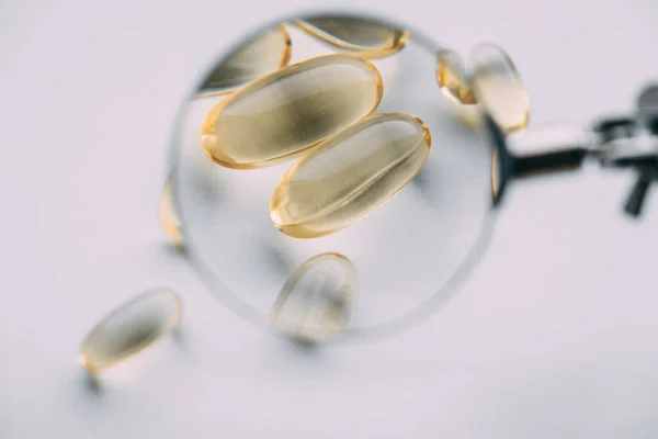 Büyüteç altında sarı şeffaf omega 3 kapsülleri. vitamin geliştirme kavramı