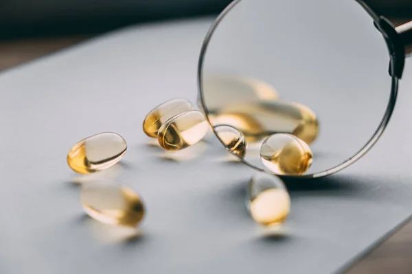 Büyüteç altında sarı şeffaf omega 3 kapsülleri. gıda katkı maddesi geliştirme kavramı