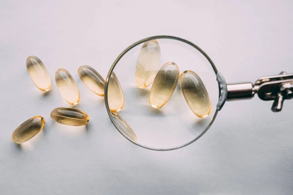 Büyüteç altında sarı şeffaf omega 3 kapsülleri. gıda katkı maddesi geliştirme kavramı