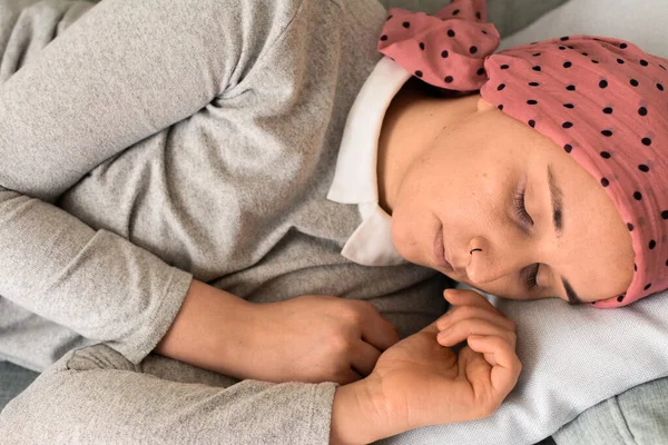 Portrait of a woman with cancer and depression locked in her home thinking. Pink headscarf. Lying on the sofa sleeping. Fighting cancer.